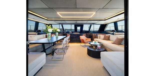 Modern salon with dining table, cushioned seating, and panoramic windows overlooking the sea.