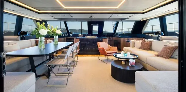 Modern salon with dining table, cushioned seating, and panoramic windows overlooking the sea.