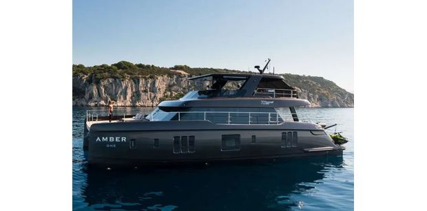 Side view profile of AMBER ONE anchored in calm blue water beside a rocky coastline