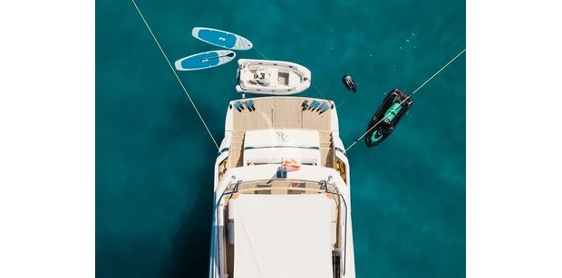 ZATARA II Sanlorenzo SL90A - aerial view of the stern and swim platform of ZATARA II anchored in turquoise waters, surrounded by water toys including paddleboards, a tender, a jet ski, and snorkeling gear.