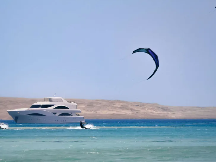 SEVEN SPICES 39-meter Custom Aluminum Cutter - anchored with windsurfing in the background SEVEN SPICES 39-meter Custom Aluminum Cutter - anchored with windsurfing in the background