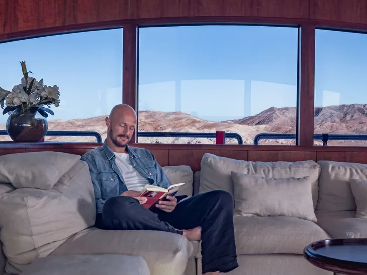 SEVEN SPICES 39-meter Custom Aluminum Cutter - guest lounging in the main saloon couch with a book SEVEN SPICES 39-meter Custom Aluminum Cutter - guest lounging in the main saloon couch with a book