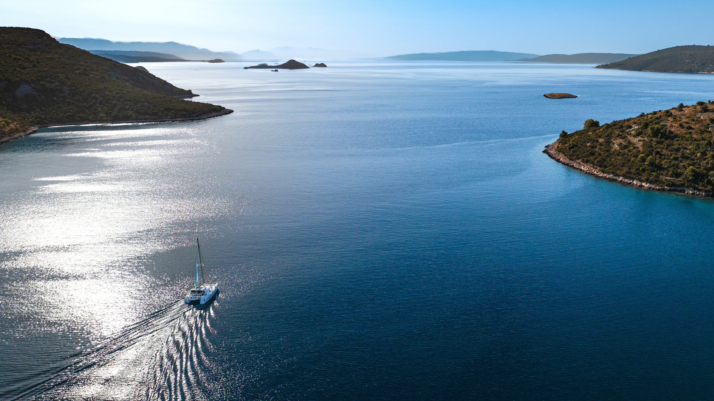 a catamaran cruising between croatian islands under the sun with the light reflecting in the water