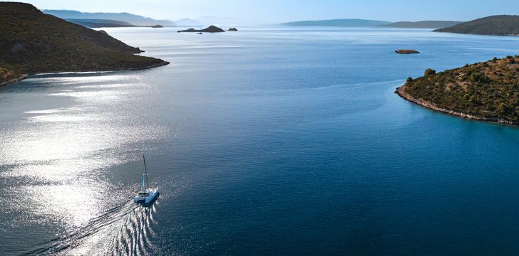 a catamaran cruising between croatian islands under the sun with the light reflecting in the water